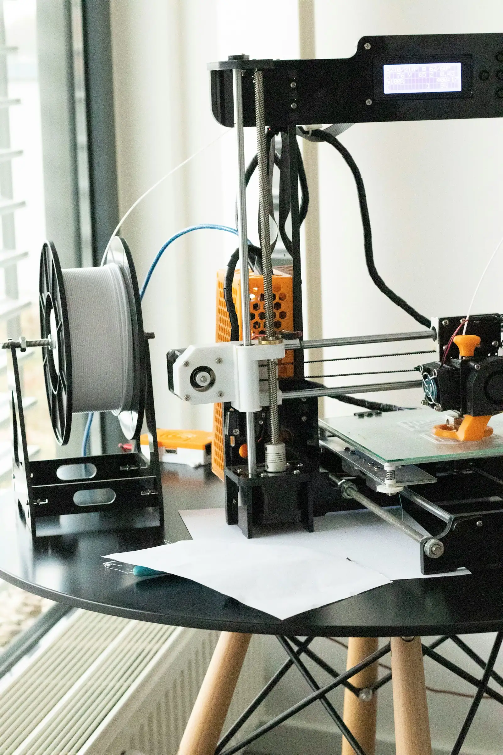 A beginner friendly desktop 3D printer with a white filament spool on a small table